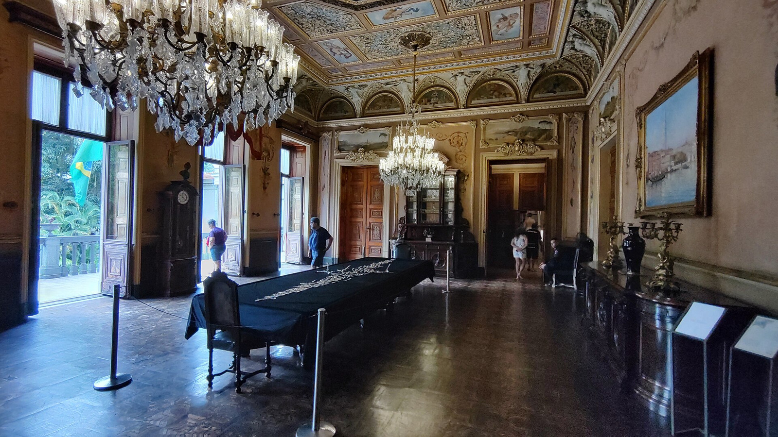 Decorated room at Palácio do Catete with a long table, chandeliers, painted ceiling, and open balcony doors