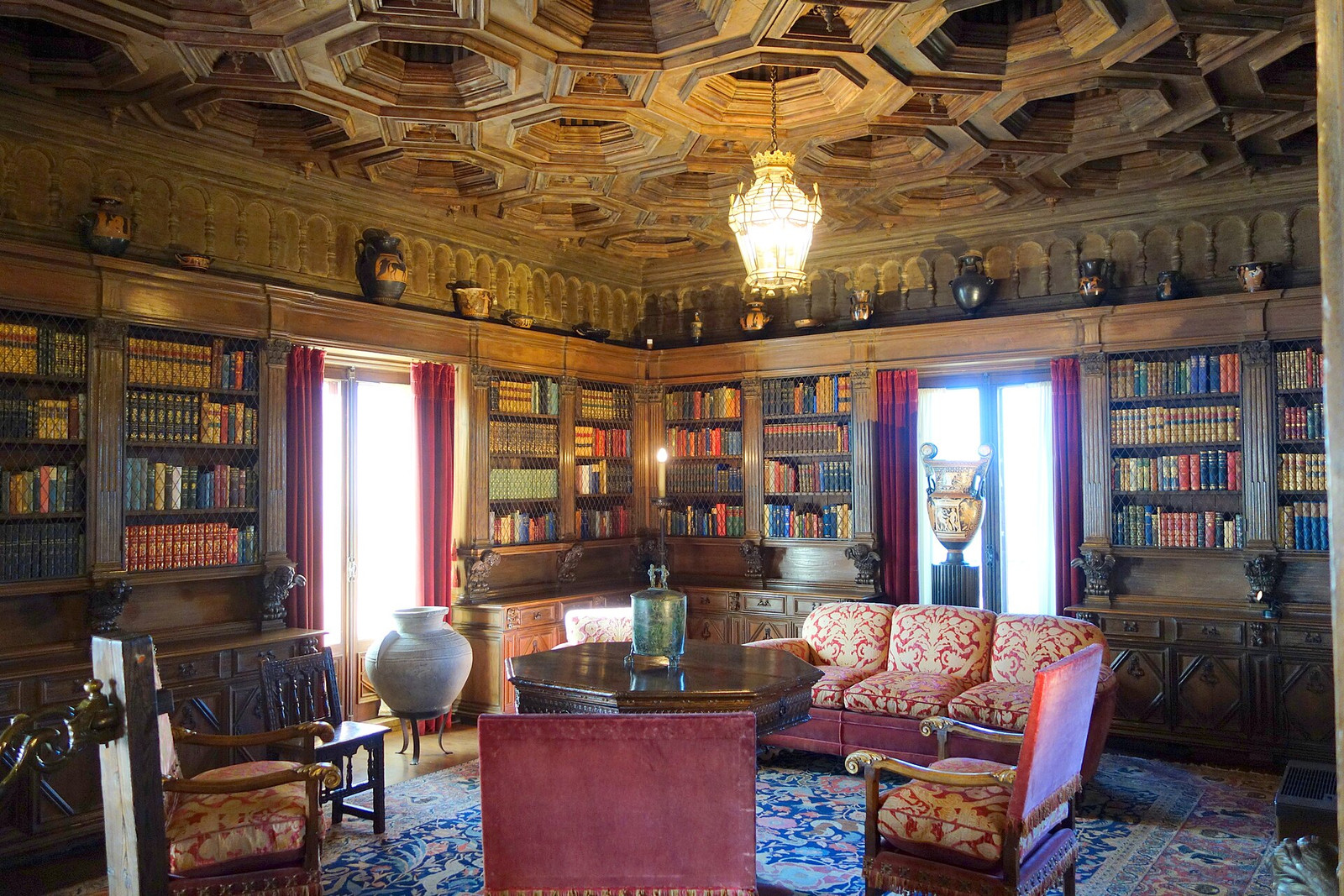 Library at Hearst Castle with books, carved ceiling panels, seating, and classical vessels