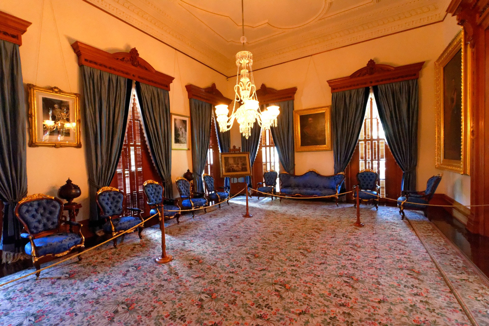 Blue Room at ʻIolani Palace with blue upholstered chairs, portraits, and tall draped windows