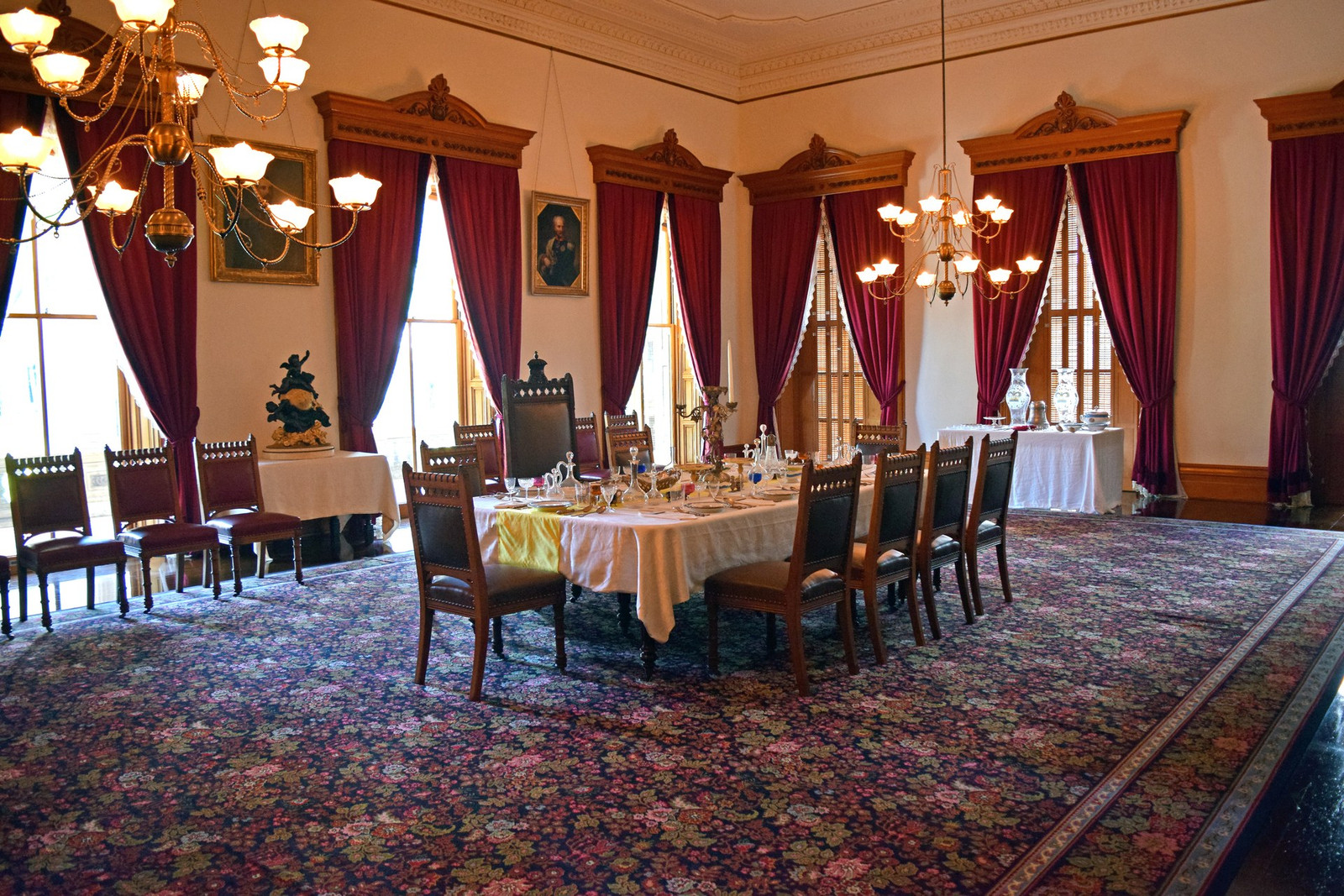 State Dining Room at ʻIolani Palace with long table, portraits, chandeliers, and tall windows