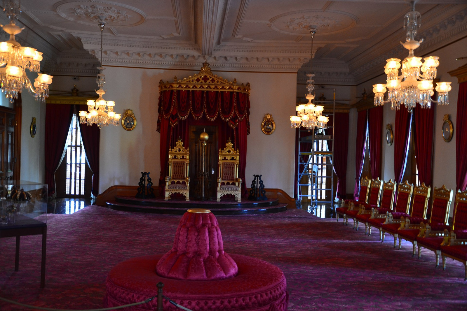 ʻIolani Palace Throne Room with crimson carpet, gilded chairs, chandeliers, and tall draped windows