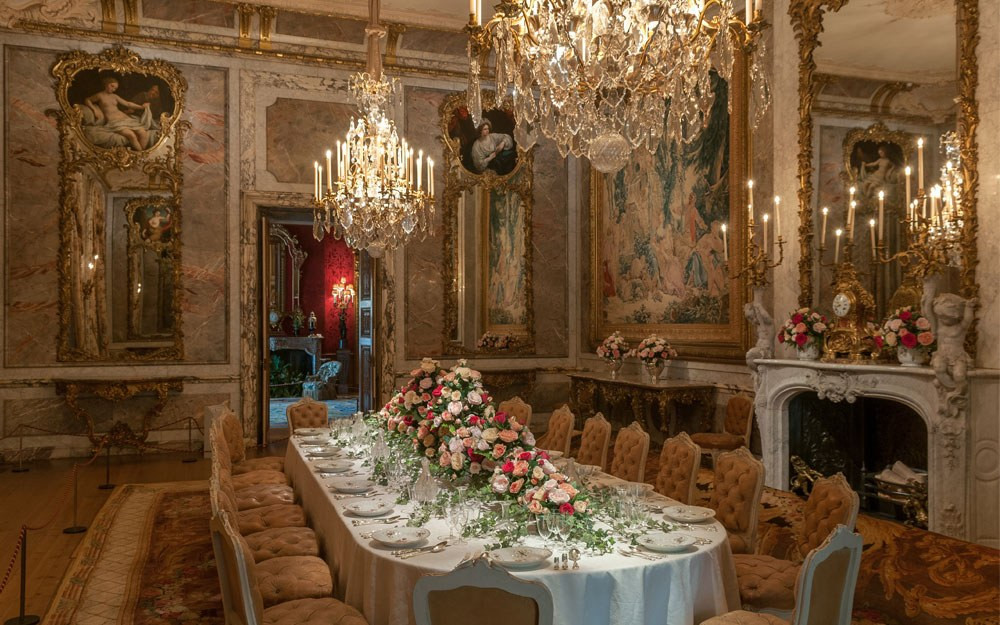 Dining room at Waddesdon Manor with a long set table, tapestries, portraits, and chandeliers