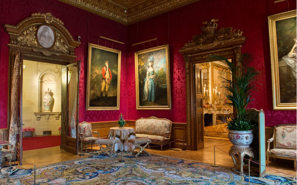 Red Drawing Room at Waddesdon Manor with crimson walls, paintings, gilt furniture, and chandeliers